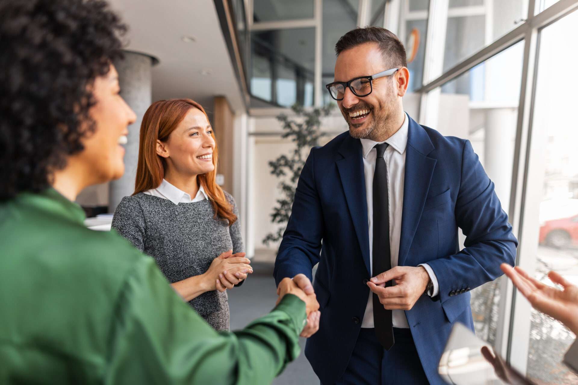 Team members in formal attire engaging in a friendly handshake, symbolizing cooperation and collaboration in a professional office environment.